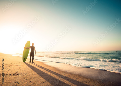 Photography Surfer on the beach holding is surfboaerd and watching the waves