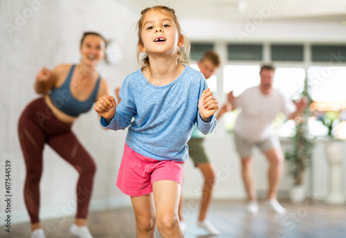 Fototapeta Naklejka Na Ścianę i Meble -  Cute little girl practicing dance movements together with her parents and brother during training session