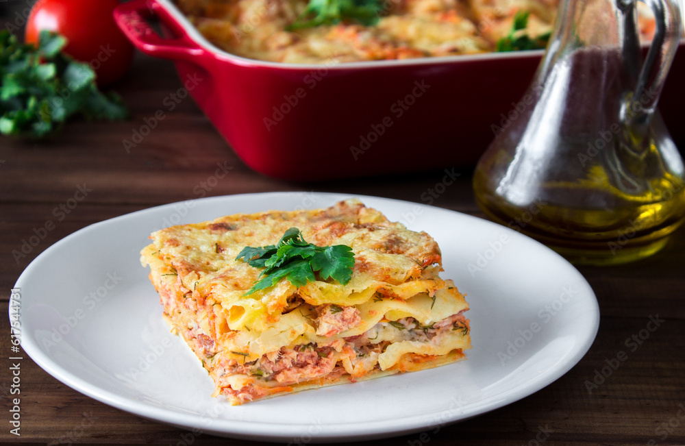 Close-up of a traditional lasagna topped with parskey leafs served on a white plate on dark wooden table Close-up of a traditional lasagna topped with parskey leafs served on a white plate on dark wooden table