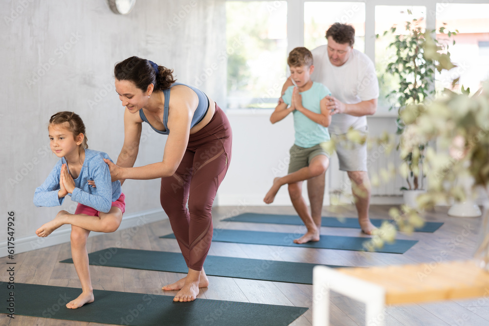 Mom and dad help their little kids in various yoga poses in the gym