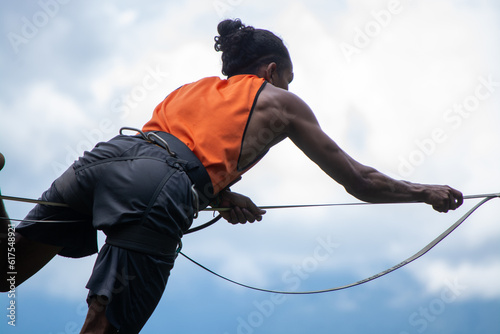 Man using harness hanging on a slackline or tightrope with man bum and orange shirt photo