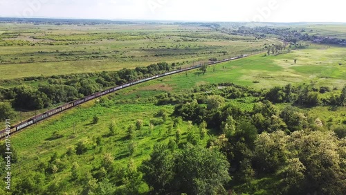 Freight-long trains carry with carriages a locomotive by the arid hilly landscape. Aerial drone perspective view at summer sunset.