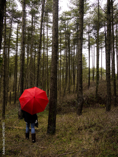 Woman walking through the woods with a red umbrella.