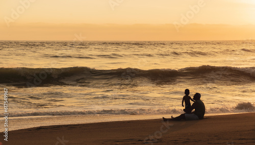 Padre e hijo sentados frente al mar a contraluz en un atardecer de verano, niño jugando y corriendo frente al mar. sunset, verano, vacaciones.