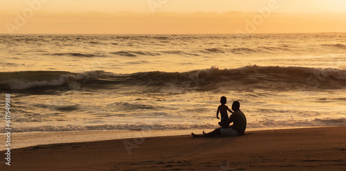 Padre e hijo sentados frente al mar a contraluz en un atardecer de verano, niño jugando y corriendo frente al mar. sunset, verano, vacaciones.