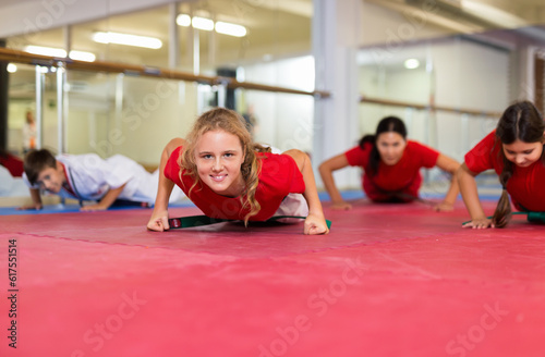 Group of teenagers together with female trainer doing warm-up and push-ups in the gym