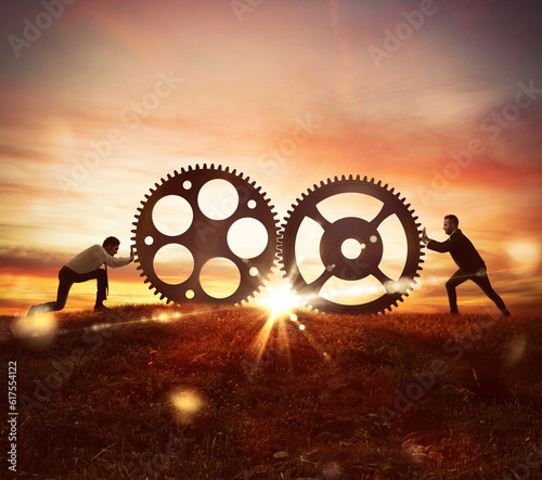 Men push two gears at sunset on mountain. Cooperation at work concept