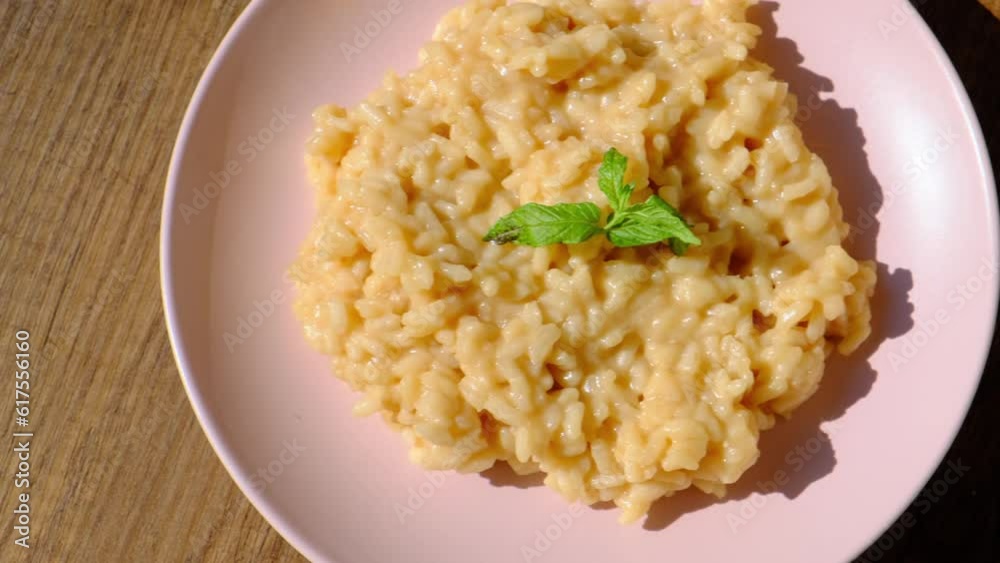 Risotto pilaf with parmesan cheese on pink plate on wooden background,slow motion Risotto pilaf with parmesan cheese on pink plate on wooden background,slow motion
