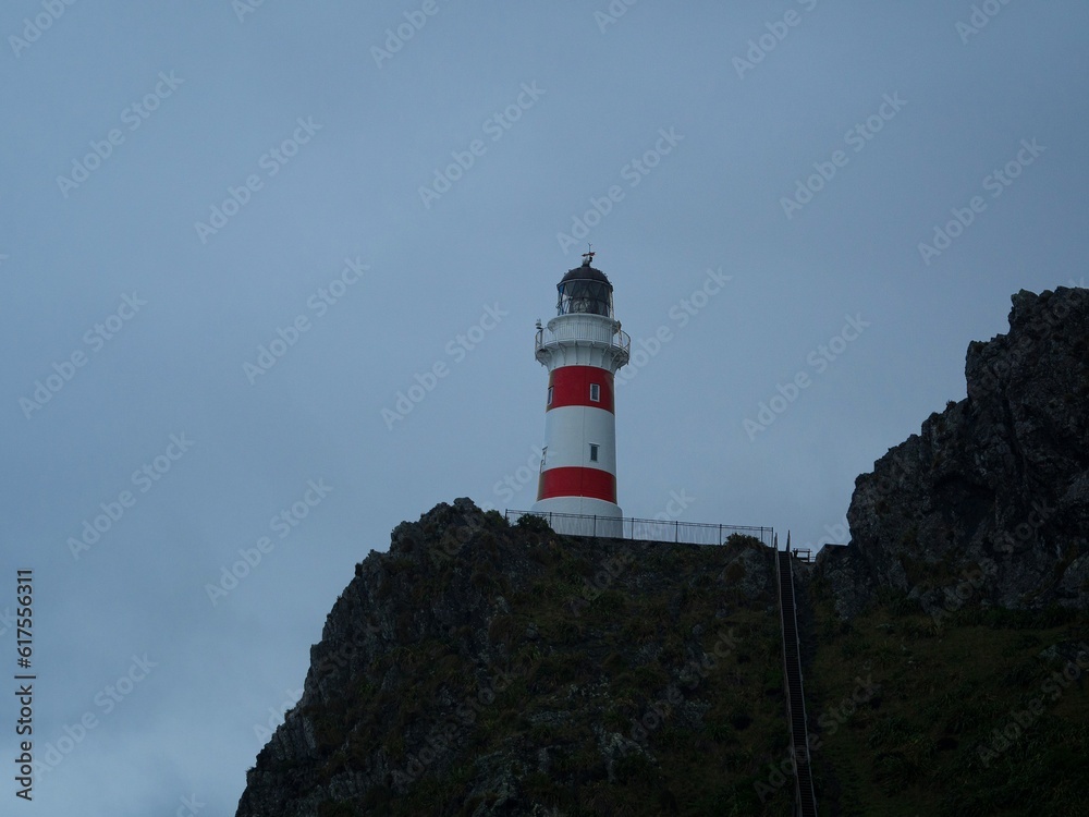 Panorama view of red and white stripes lighthouse on top of oceanside cliff hill, Cape Palliser Wellington New Zealand
