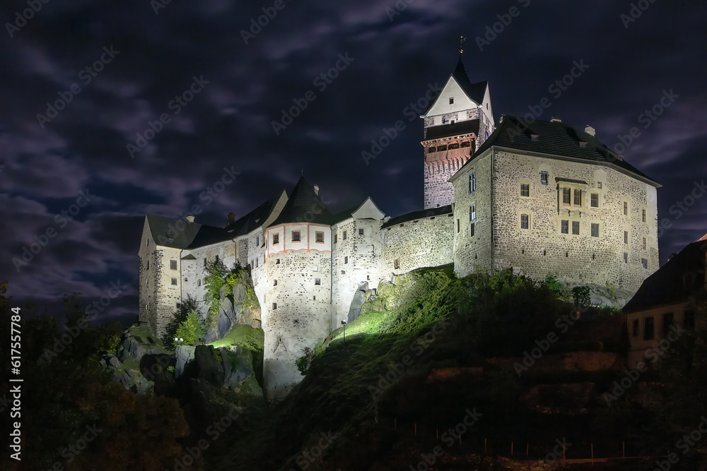 Loket Castle is a 12th-century Gothic style castle located about 12 km from Karlovy Vary on a massive rock in the town of Loket, Czech Republic. Evening Loket Castle is a 12th-century Gothic style castle located about 12 km from Karlovy Vary on a massive rock in the town of Loket, Czech Republic. Evening