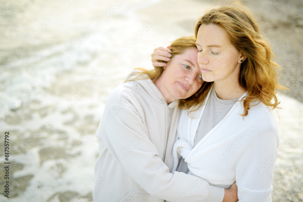 Obraz premium Redhead senior mother and her beautiful adult daughter are walking together and embracing. Family relationships between adult children and older parents