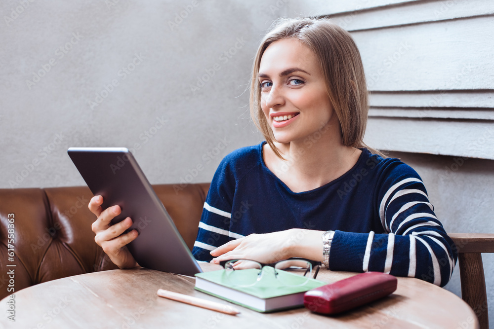 Beautiful young woman sitting in cafe and use tablet. Smiling and looking at camera. Consept of studing and working online. Beautiful woman with digital tablet, while relaxing after work Beautiful young woman sitting in cafe and use tablet. Smiling and looking at camera. Consept of studing and working online. Beautiful woman with digital tablet, while relaxing after work