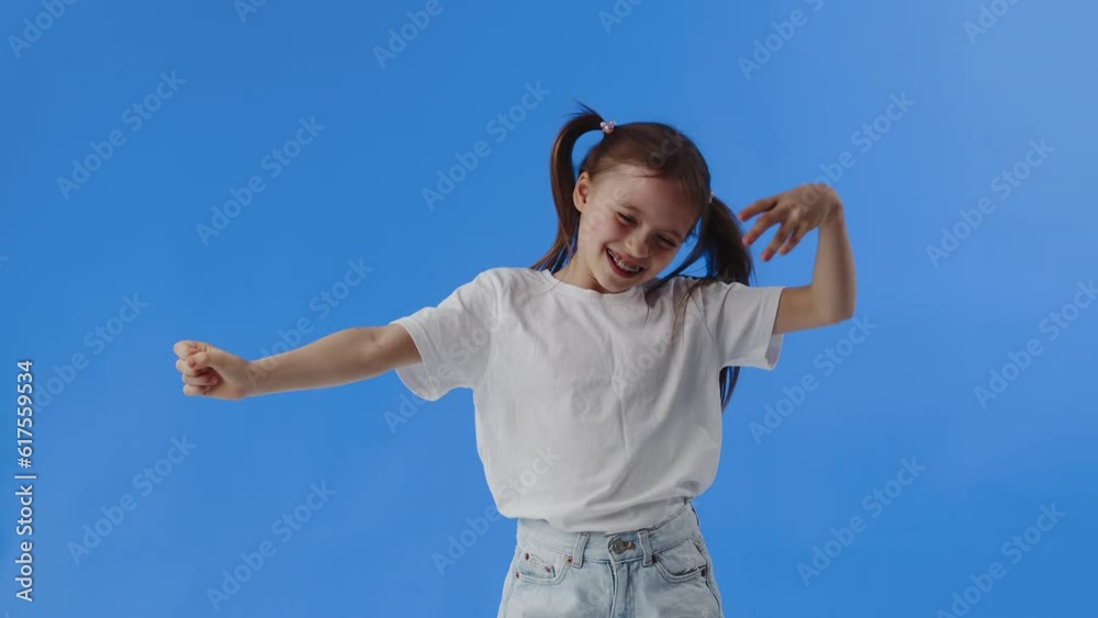 Happy young girl cheerfully smiling, funny dancing and grimacing on blue background. Concept of interesting leisure and useful entertainment for active kids Happy young girl cheerfully smiling, funny dancing and grimacing on blue background. Concept of interesting leisure and useful entertainment for active kids