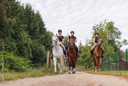 Three horsewomen enjoy riding beautiful horses, side by side along the trail at the equestrian center on a sunny day
