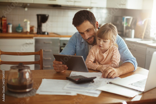 Single father using a digital tablet with his daughter in the morning while going over bills © Geber86