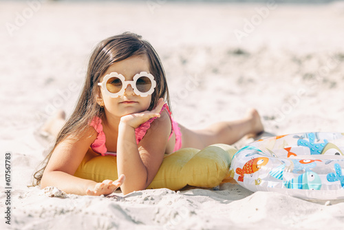 Happy cute smiling little girl in sunglasses lying on the sand on a beach in a swimsuit. Summer concept