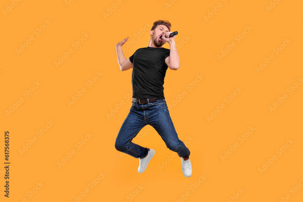 Fototapeta premium Handsome man with microphone singing and jumping on yellow background