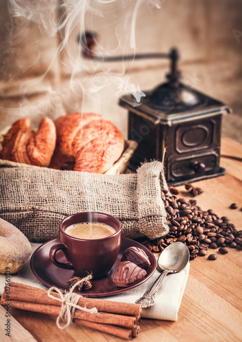 Cup fragrant hot coffee with bean chocolate sweet and croissant in vintage rustic style cinnamon steam smoke on wooden board for bracing morning breakfast.