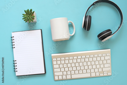 Creative composition top view with headphone, keyboard, succulent, white mug mockup and copy space on blank notebook page