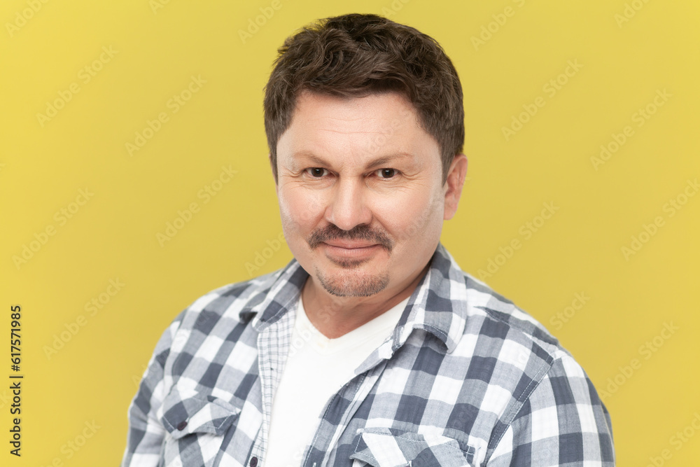 Portrait of smiling middle aged man in casual checkered shirt with beard and mustache looking at camera with positive expression. Indoor studio shot isolated on yellow background. Portrait of smiling middle aged man in casual checkered shirt with beard and mustache looking at camera with positive expression. Indoor studio shot isolated on yellow background.