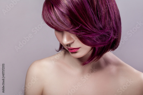 Side view portrait of calm beautiful attractive fashion model woman with short purple colored hairstyle and pink lips, looking down. Indoor studio shot isolated on gray background.