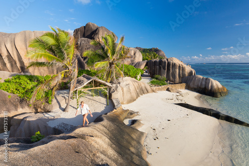 Female traveler emjoying climbing ob beautifully shaped granite boulders at picture perfect tropical Anse Source d'Argent beach, La Digue island, Seychelles.