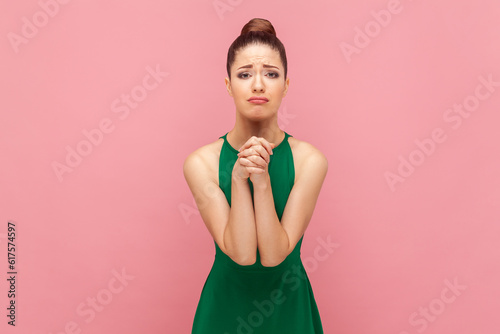 Принти на полотні Portrait of sad desperate woman with bun hairstyle standing keeps hands in praying gesture, pleading, apologizing, wearing green dress