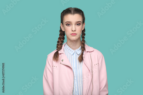 Portrait of serious strict young teenager girl with braids wearing pink jacket looking at camera with bossy expression, being in bad mood. Indoor studio shot isolated on green background. photo