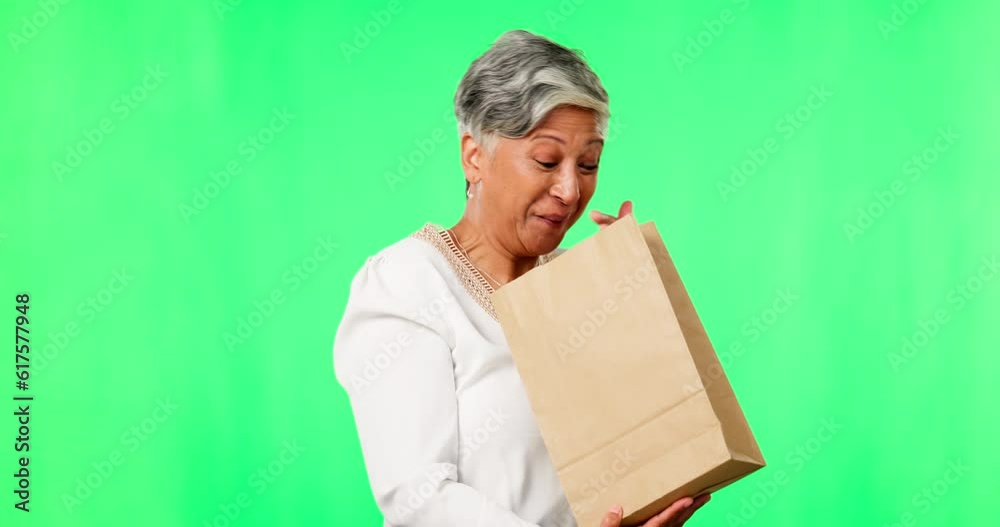 Shopping, wow and a senior woman on a green screen background in studio looking surprised or excited by a package. Retail, silly and a mature customer holding a gift, present or bag in anticipation
