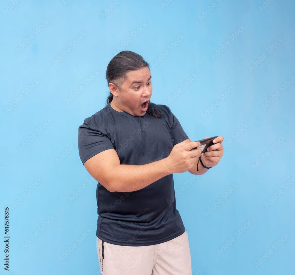 An engaged biracial male holding phone with both hands horizontally to game. Isolated on a blue background. An engaged biracial male holding phone with both hands horizontally to game. Isolated on a blue background.