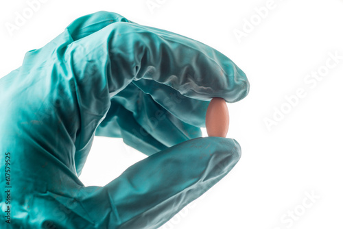 Hand with green protective glove holding an oblong pill, isolated on white background
