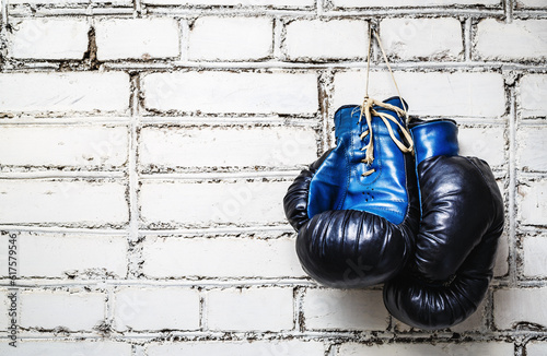Pair of old blue and black boxing gloves hanging on white brick wall. © Designpics