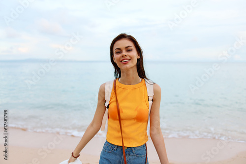 Young woman smile with teeth after swimming in the ocean with a backpack in wet clothes walking along the beach  summer vacation on the island by the ocean in Bali sunset