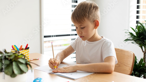 A cute boy makes a drawing with a ruler and pencil. Home lessons. Geometry and drawing.
