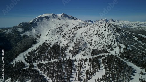 Aerial drone flyover of Mammoth Mountain ski resort in California with runs and chair lifts in view during snowy winter on clear sunny day
