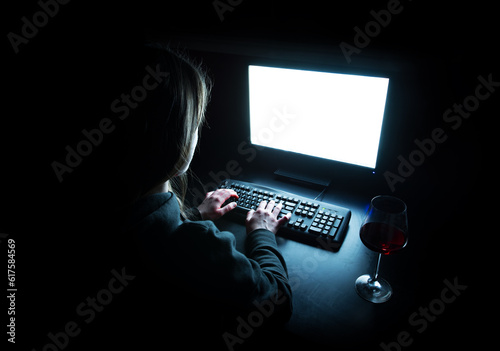 Fotografie Silhouette of woman typing at computer in dark illuminated by screen with wine g
