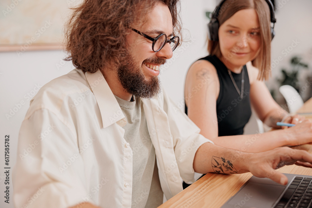 Two smiling colleagues working together on project while sitting on the desk in cozy coworking Two smiling colleagues working together on project while sitting on the desk in cozy coworking