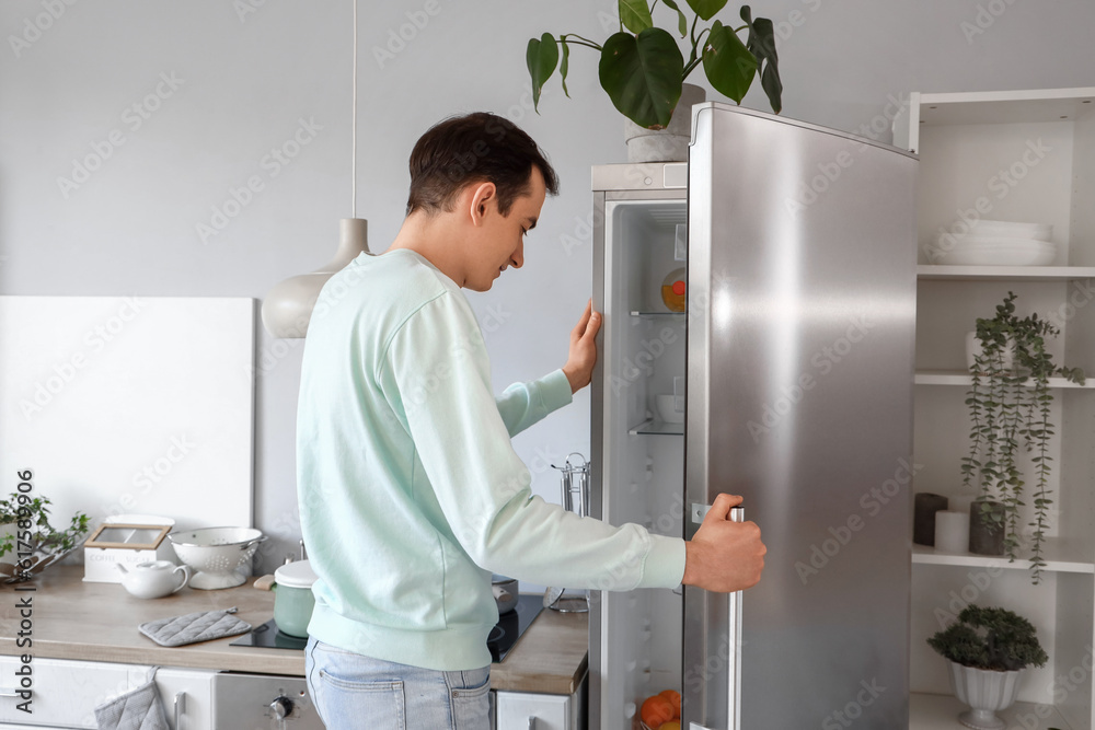 Handsome man opening fridge in kitchen