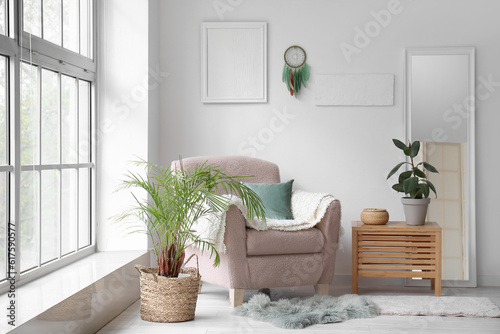 Interior of modern living room with armchair, plants and dream catcher hanging on light wall