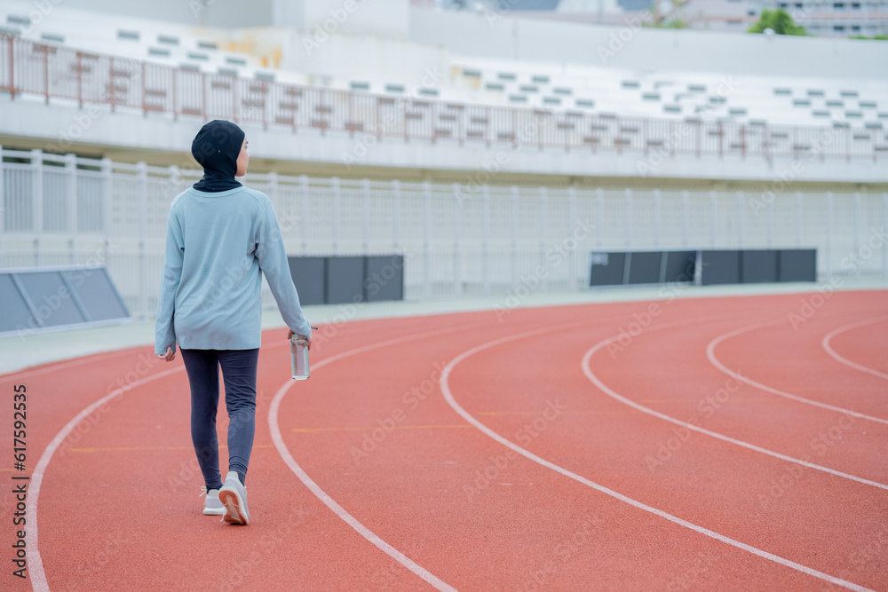 Fototapeta premium A young asian Muslim woman wearing a black hijab is exercising and running at an outdoor stadium in the morning. Modern Muslim woman concept, Muslim woman sport concept, Islam