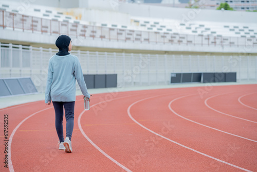 A young asian Muslim woman wearing a black hijab is exercising and running at an outdoor stadium in the morning. Modern Muslim woman concept, Muslim woman sport concept, Islam