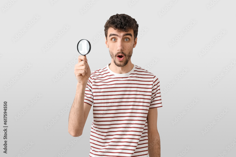 Shocked young man with magnifier on light background Shocked young man with magnifier on light background