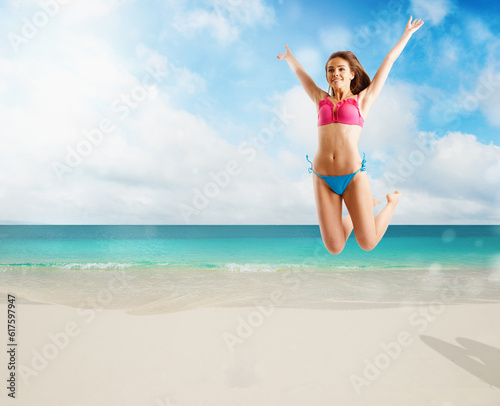 Woman in bikini swimsuit jumping from joy on tropical beach shore