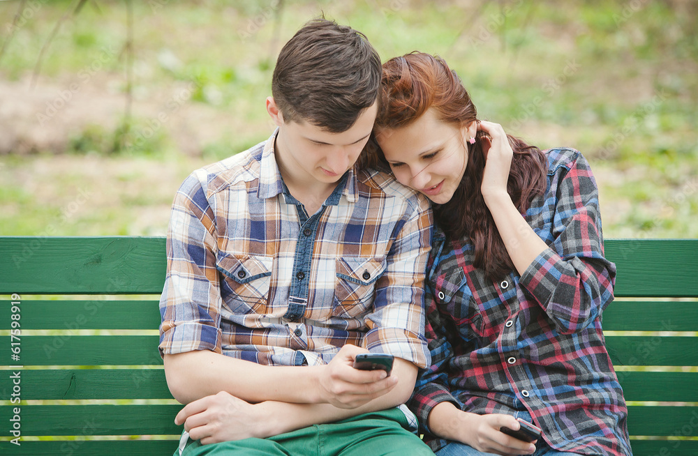 Young couple sitting on the bench at the park watching attentively at mobile phone Young couple sitting on the bench at the park watching attentively at mobile phone