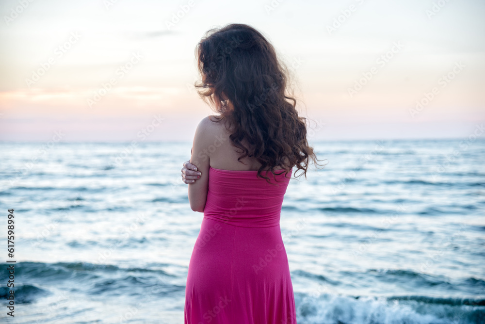 Woman in red dress standing on the sea at the sunrise Woman in red dress standing on the sea at the sunrise