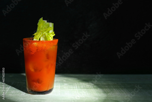 Glass of bloody mary with celery on wooden table against dark green background