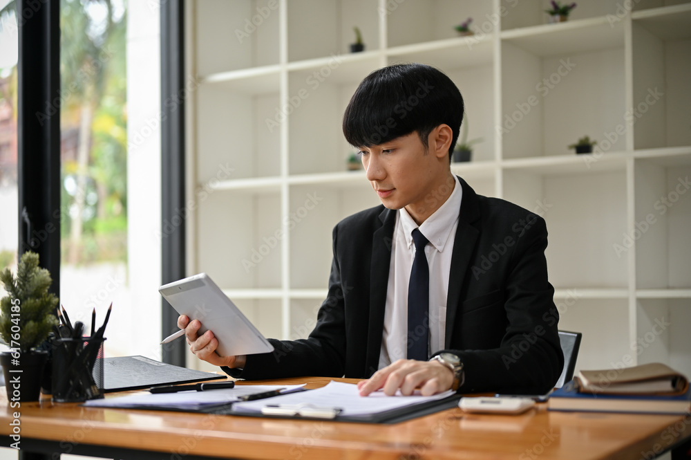 A handsome Asian male lawyer focuses on examining a notice letter at his desk. A handsome Asian male lawyer focuses on examining a notice letter at his desk.