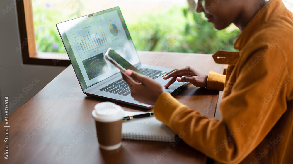 African american businesswoman working on smartphone and laptop to reading business data in cafe