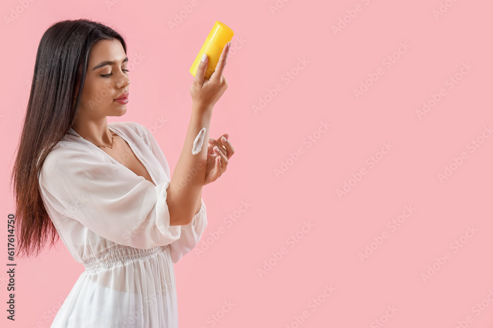 Young woman applying sunscreen cream on pink background Young woman applying sunscreen cream on pink background