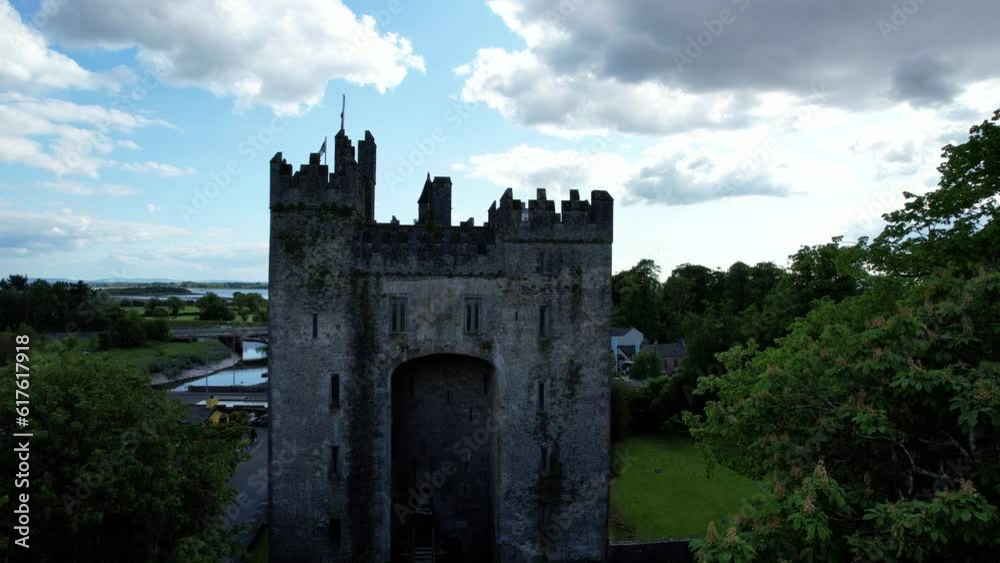 Bunratty Castle among Folk Park trees in Ireland, Atlantic Ocean in background. Aerial ascending